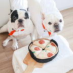 Deux bouledogues français en toque devant la poêle à pizza