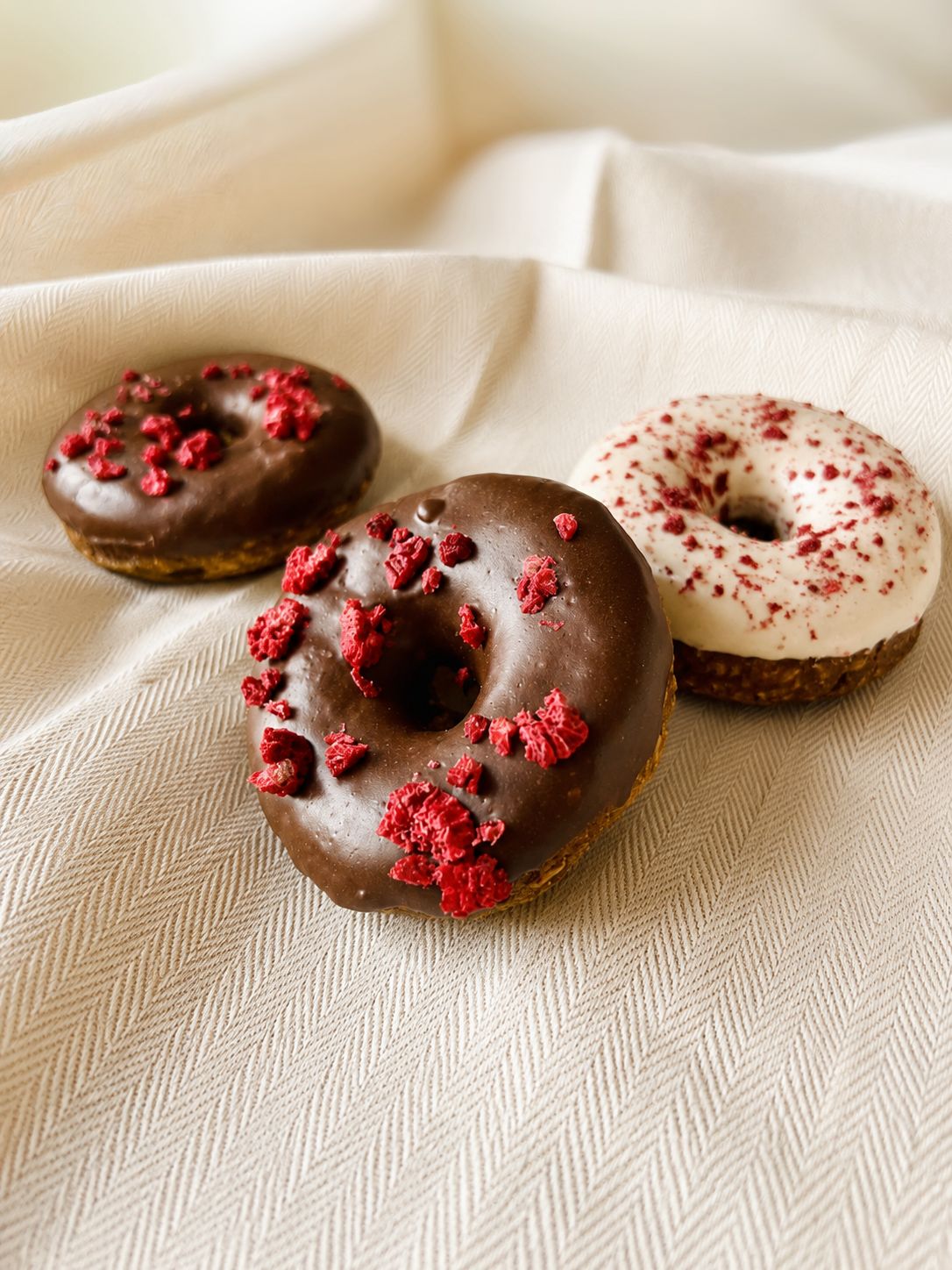 Donuts chocolat et blancs parsemés de framboise sur un drap clair